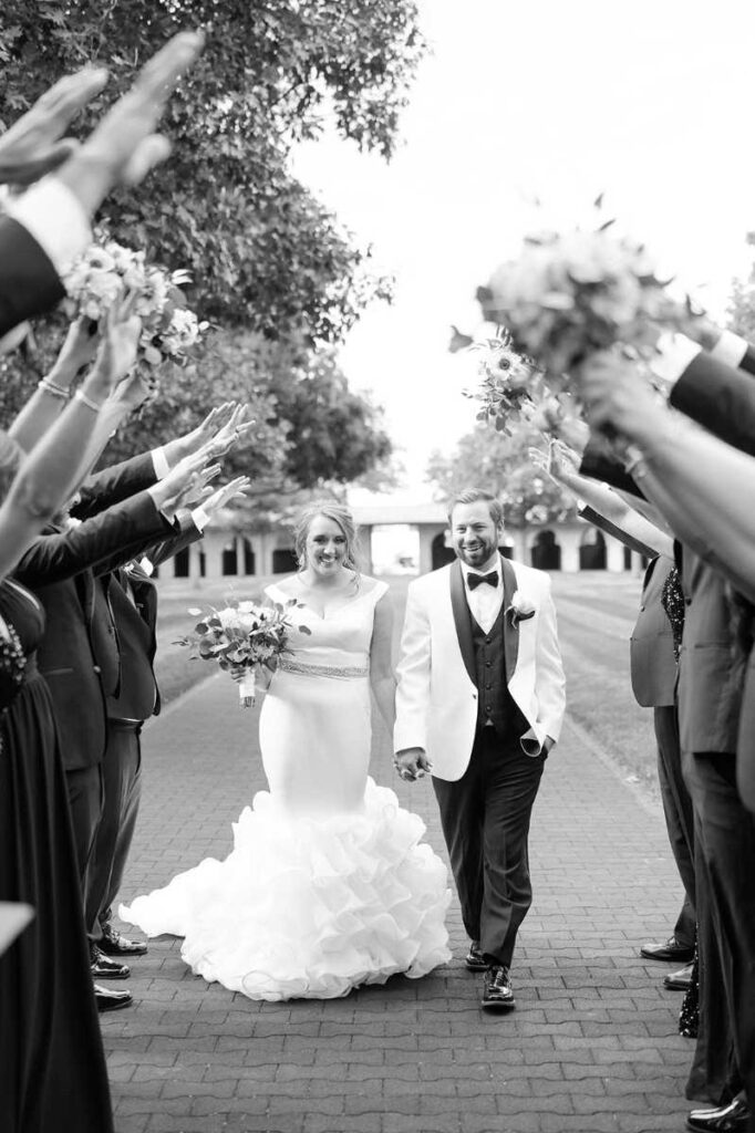 Lexington KY outdoor wedding venues – romantic couple walking through Keeneland’s courtyard surrounded by bridal party