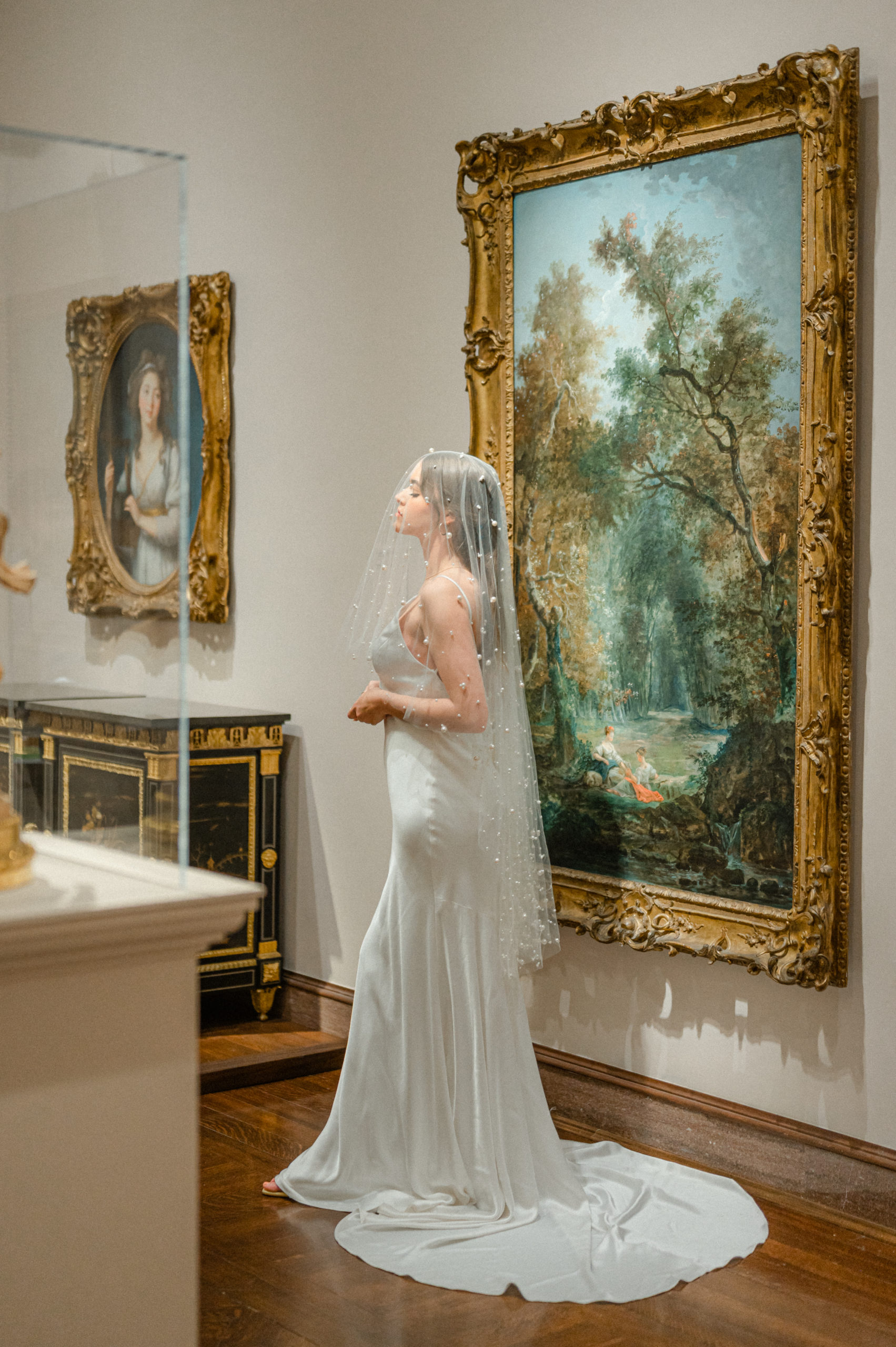 Bridal portrait inside the Cincinnati Art Museum. Bride is wearing a fitted dress with long train and a pearl veil over her head.