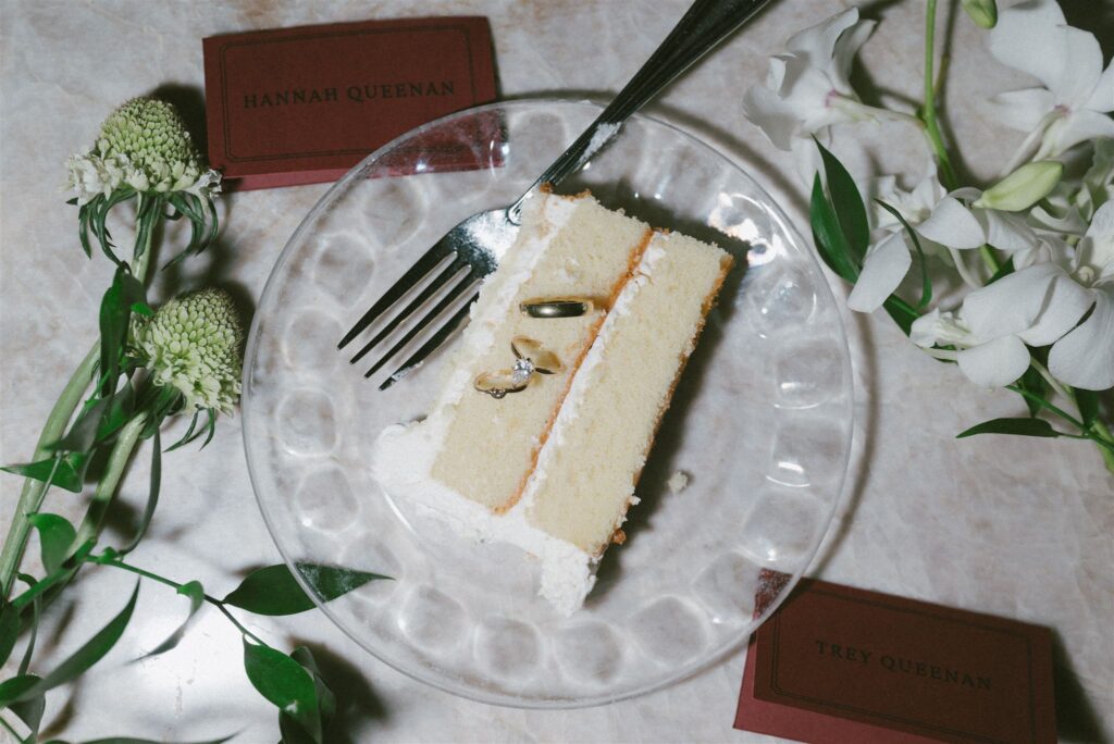 Wedding day details of cake slice and rings on a plate photographed at Lexington Country Club in  KY.