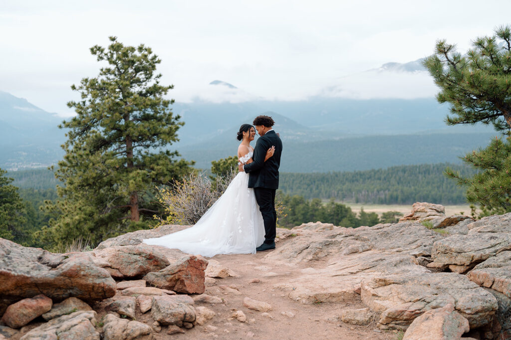 Bride and groom embracing with mountain peaks in Rocky Mountain National Park.