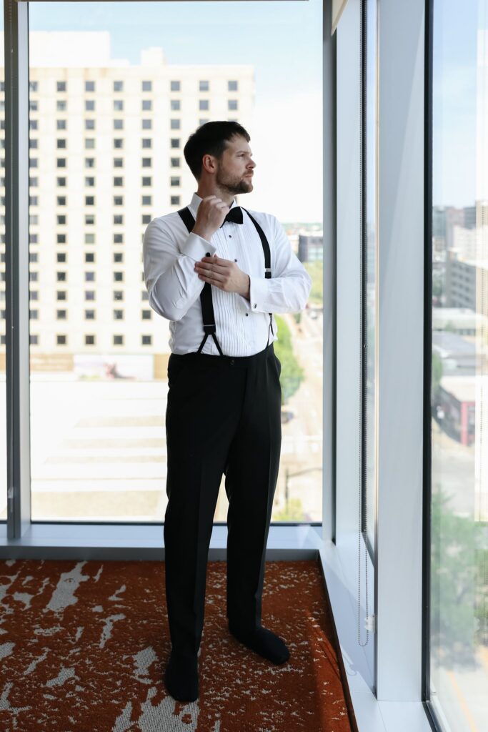 Groom getting ready by a hotel window before his wedding at The Olmsted Louisville.