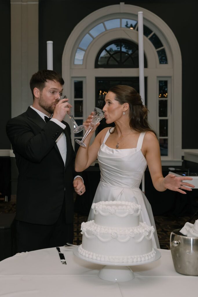 Bride and groom toasting with champagne beside their wedding cake during their The Olmsted Louisville wedding reception.