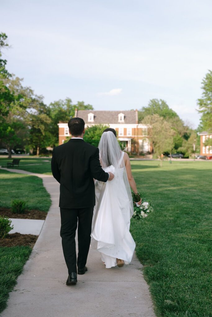 Bride and groom walking hand in hand across the lawn after portraits at The Olmsted in Louisville.
