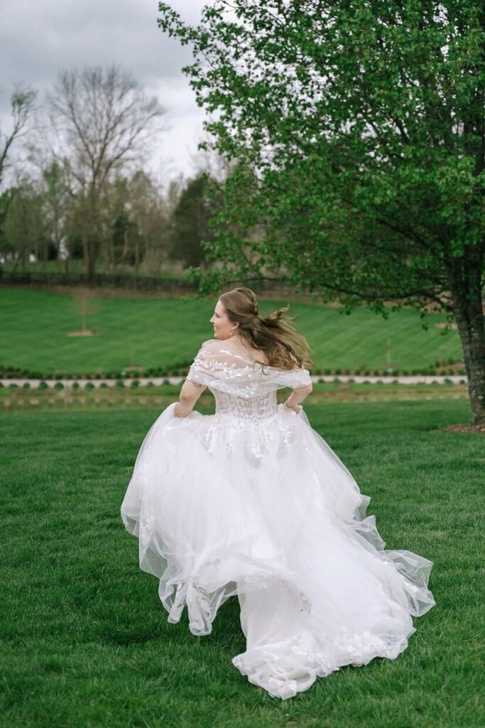 Bride running in a beautiful grass lawn with her dress billowing behind her at Hazelnut Farms, a venue for outdoor weddings in Louisville. 