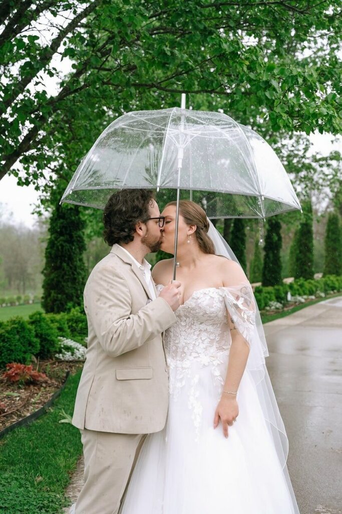 Bride and groom kissing under an umbrella at Hazelnut Farms, an outdoor wedding venue in Louisville, KY.