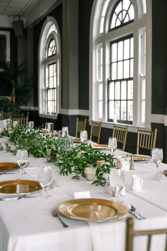 Table set for reception with greenery and elegant golden plates at The Olmstead, an indoor-outdoor wedding venue in Louisville. 