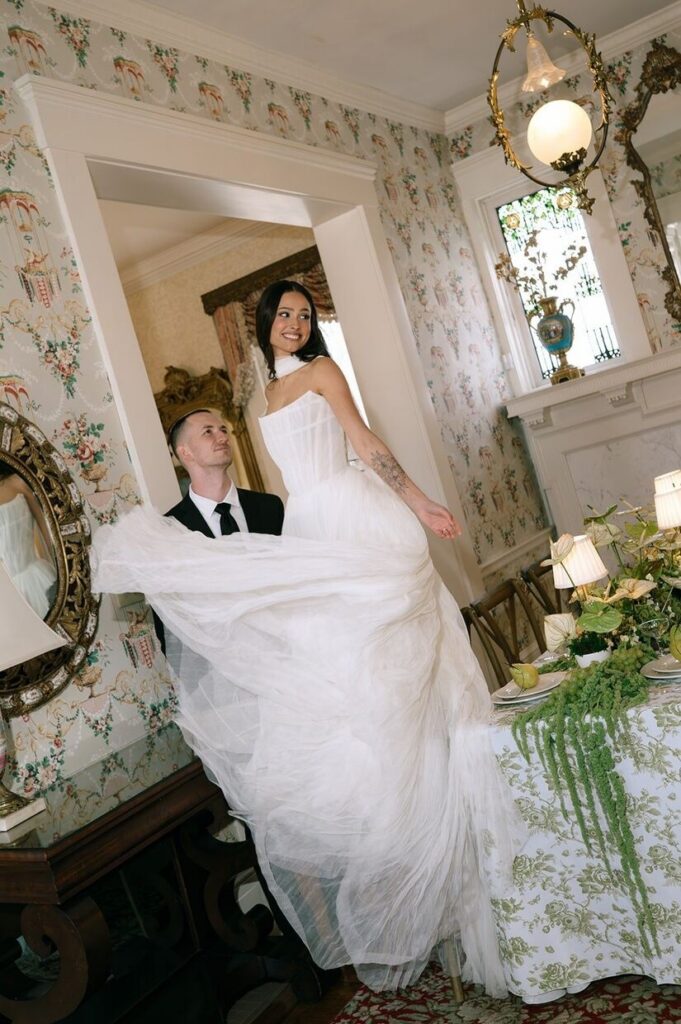 Groom looking at bride as she tosses her wedding dress in a charming hallway in Whitehall, a venue for outdoor weddings in Louisville. 
