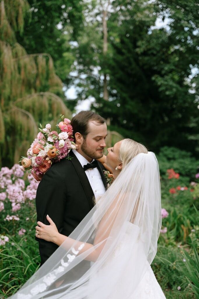 Bride and groom looking at one another with a beautiful garden behind them at Whitehall, an outdoor wedding venue in Louisville. 
