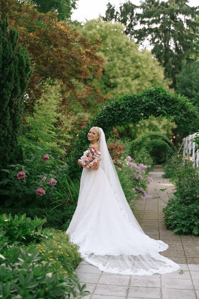 Bride looking over her shoulder and smiling in the gardens at Whitehall wedding venue. 