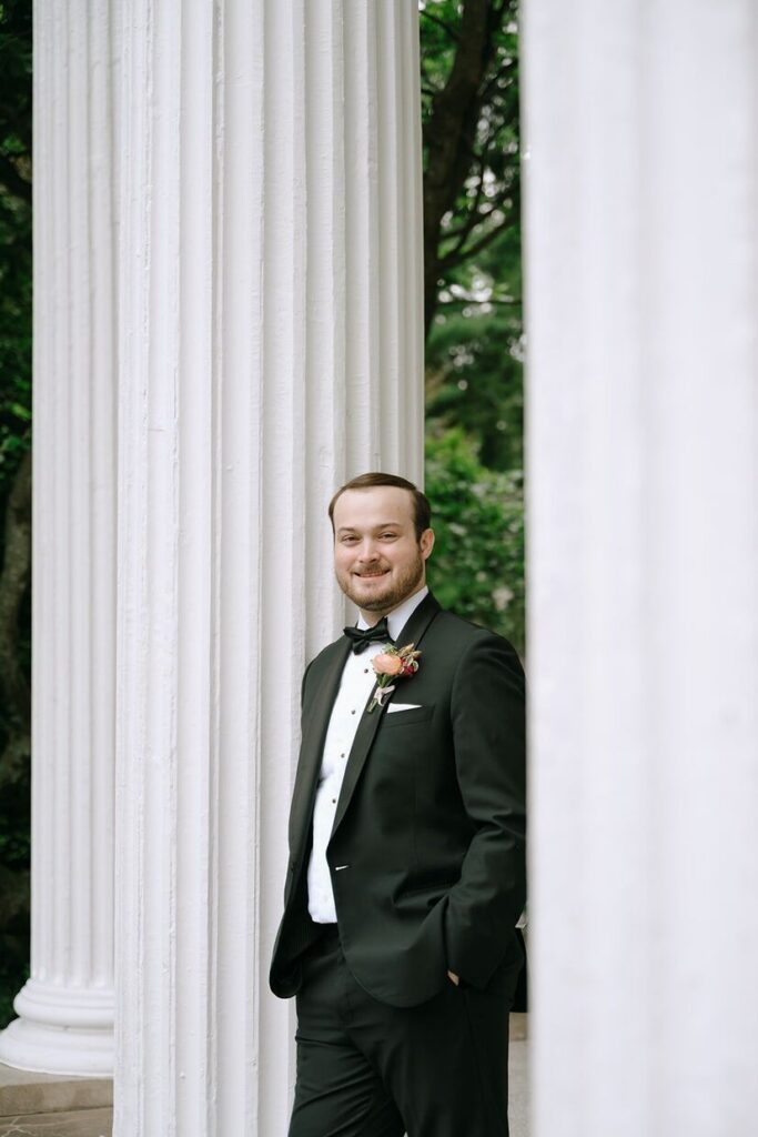 Groom smiling at camera in between elegant columns at the Whitehall mansion wedding venue. 